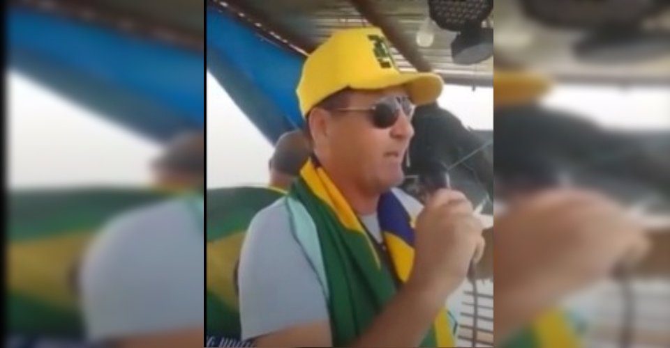 Homem de boné amarelo, óculos escuro e segurando microfone