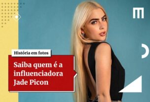 Na imagem colorida, uma mulher está posicionada à esquerda.  Ela usa roupas pretas, tem cabelos longos loiros e olha seriamente para a câmera sobre os ombros