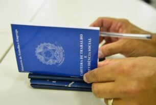 foto mostra duas mãos segurando uma carteira de trabalho e uma caneta